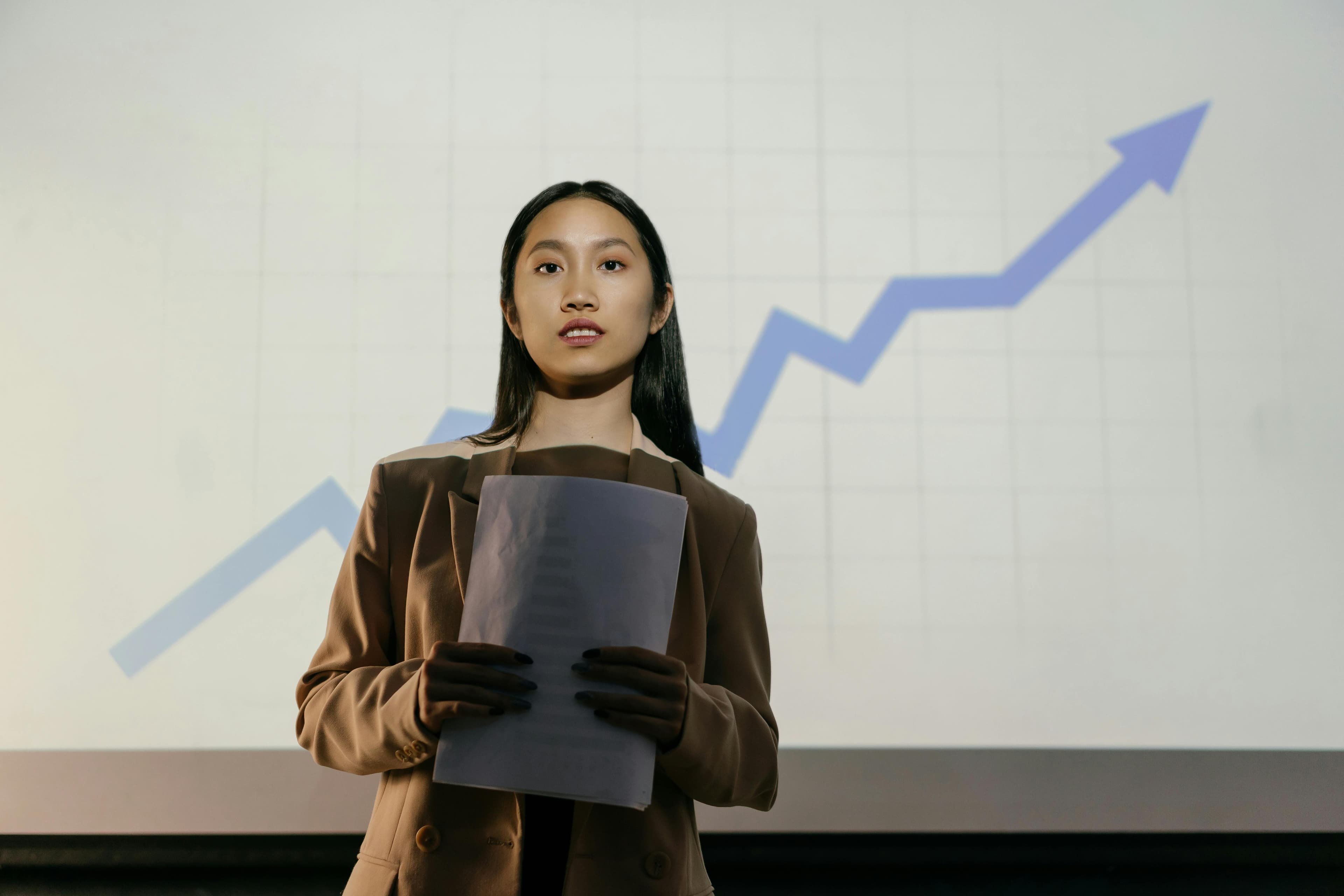Professional businesswoman holding documents with upward trending growth chart in background representing business success and financial growth